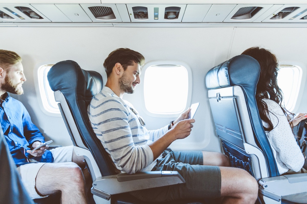 Young man sitting inside an airplane and using a digital tablet. Male passenger using e-reader during flight.