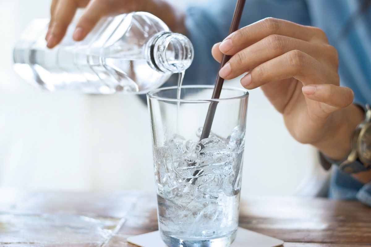 person pouring ice water into glass