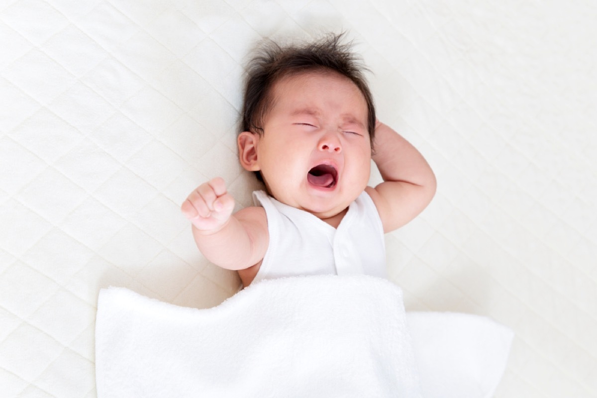 newborn asian baby crying in bed with white sheets