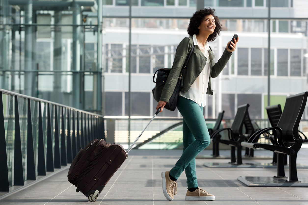 A young woman pulling her suitcase through the airport while using her phone