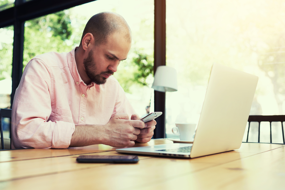 A man using an Android phone while sitting at his laptop computer