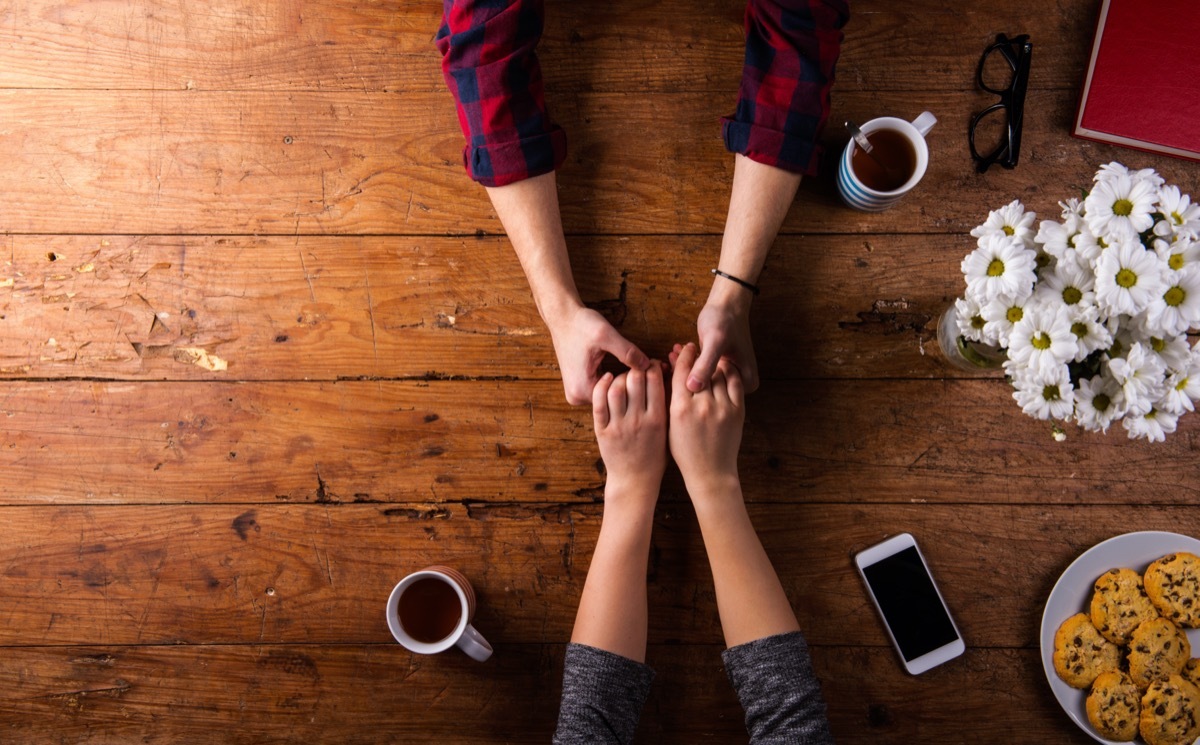 overhead shot of a man and woman holding hands on a wooden table top