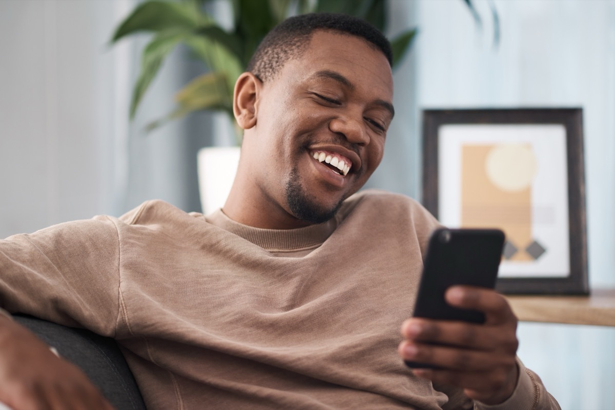 man smiling while reading funny quotes on his cell phone