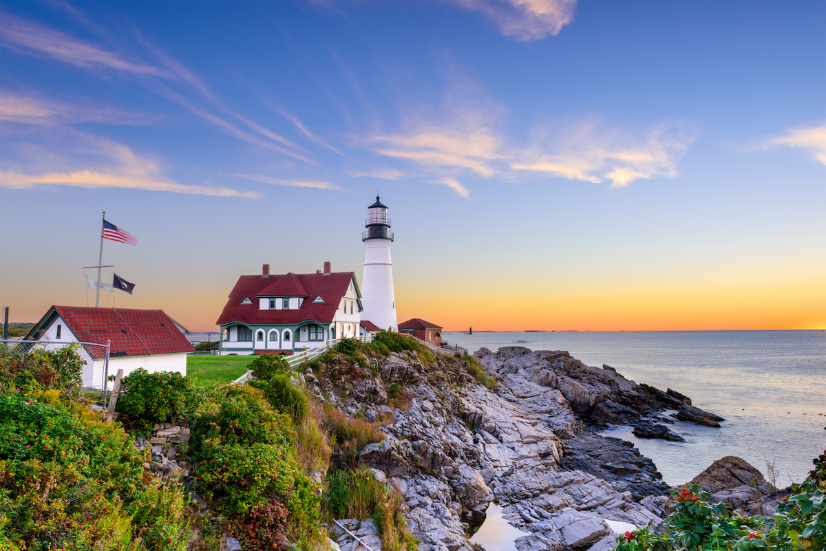 Maine's Portland Head Lighthouse at dusk, with rocky cliffs in the foreground.