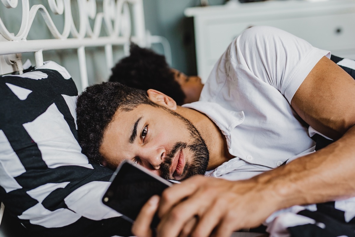 Young men is laying in bed next to his girlfriend and uses smart phone