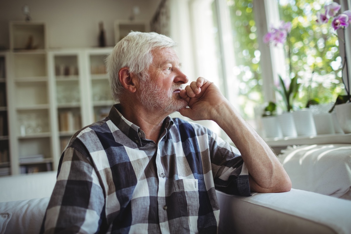 Thoughtful senior man sitting on sofa at home