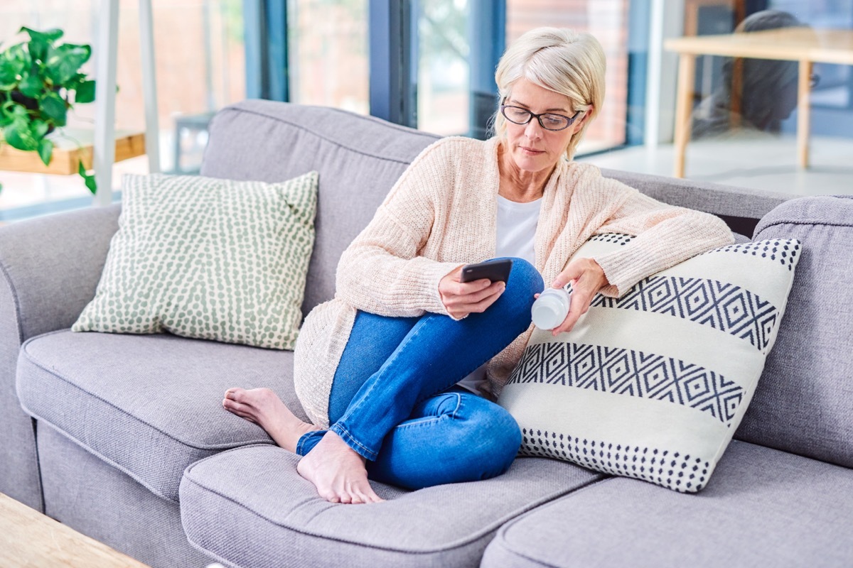 Shot of a senior woman using a smartphone and reading the label on a medicine container at home