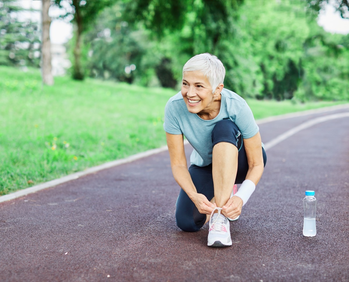 Portrait of a happy active beautiful senior woman posing fixing shoelace on her running shoe after exercising outdoors