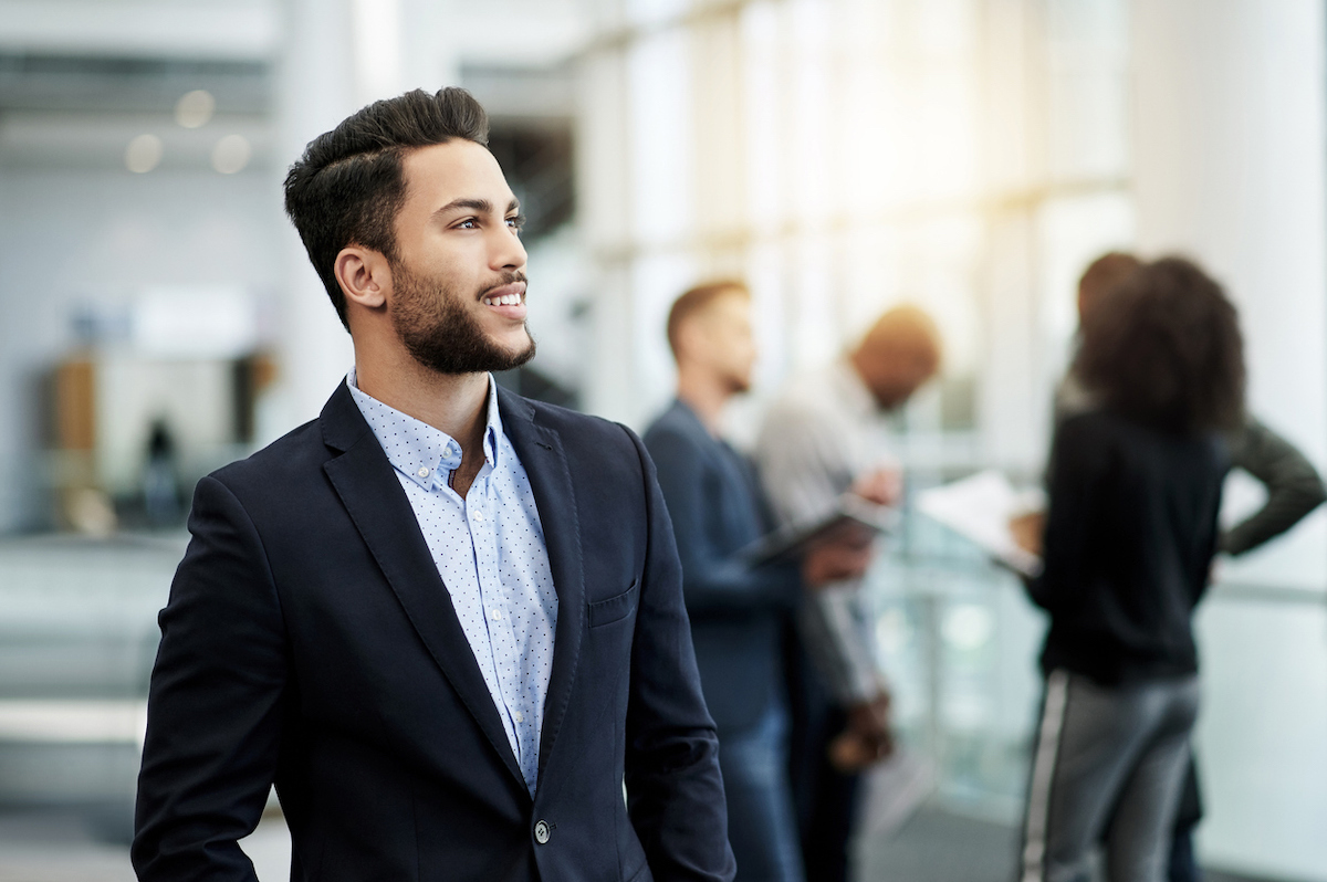 Shot of a confident young businessman looking thoughtful in an office with his colleagues in the background