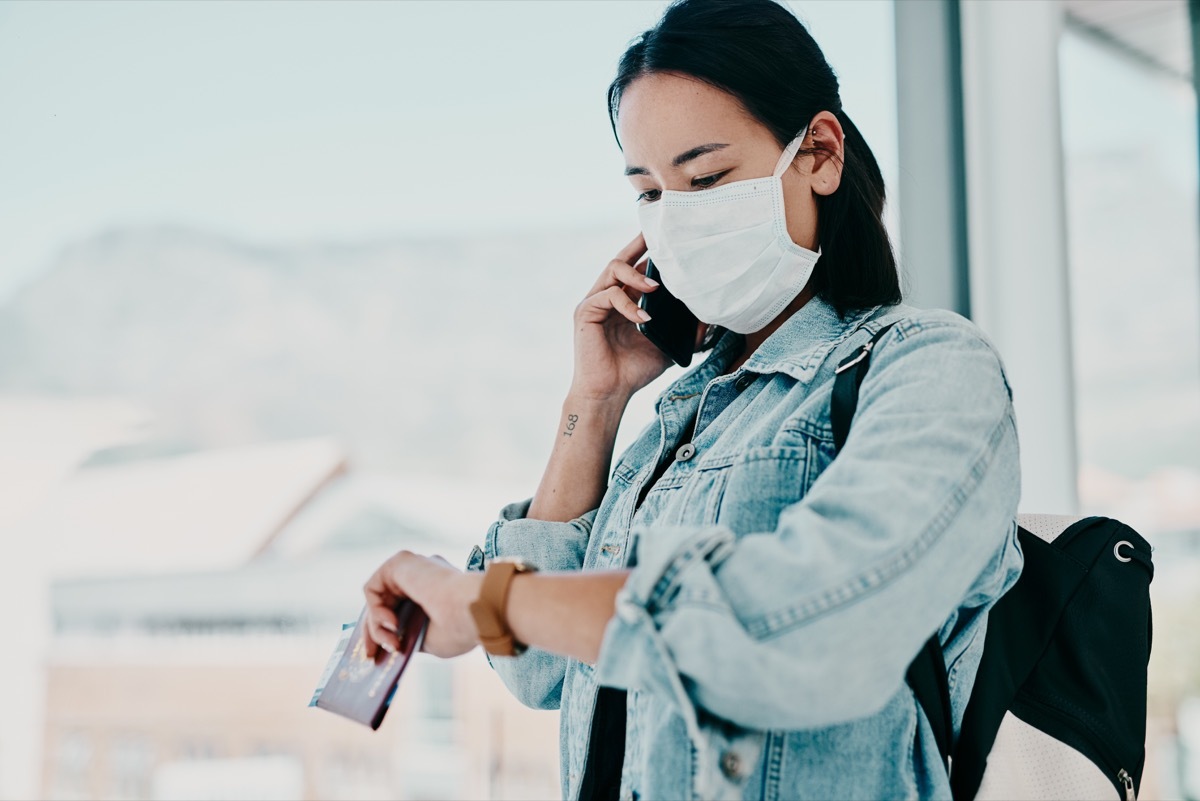 Shot of a young woman wearing a mask, using a smartphone and checking the time in an airport