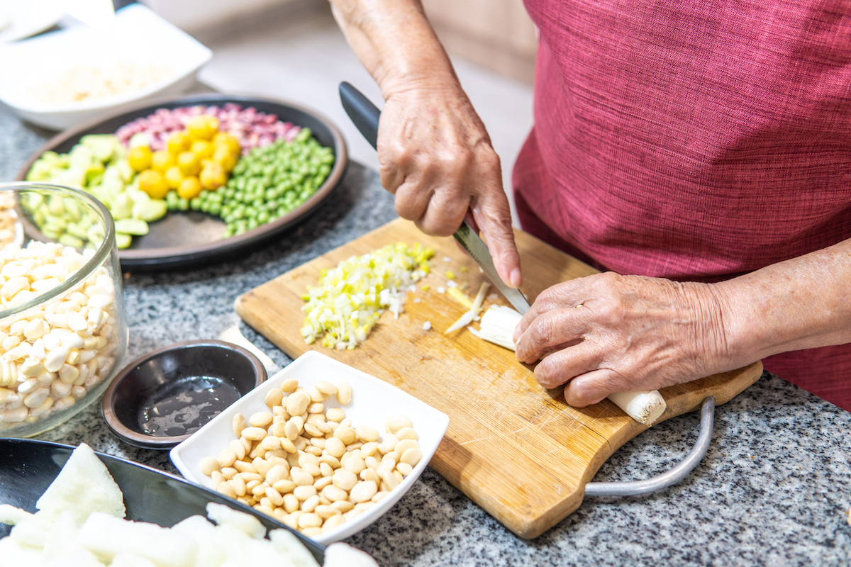 Hands of an elderly woman cutting onions with several legumes.