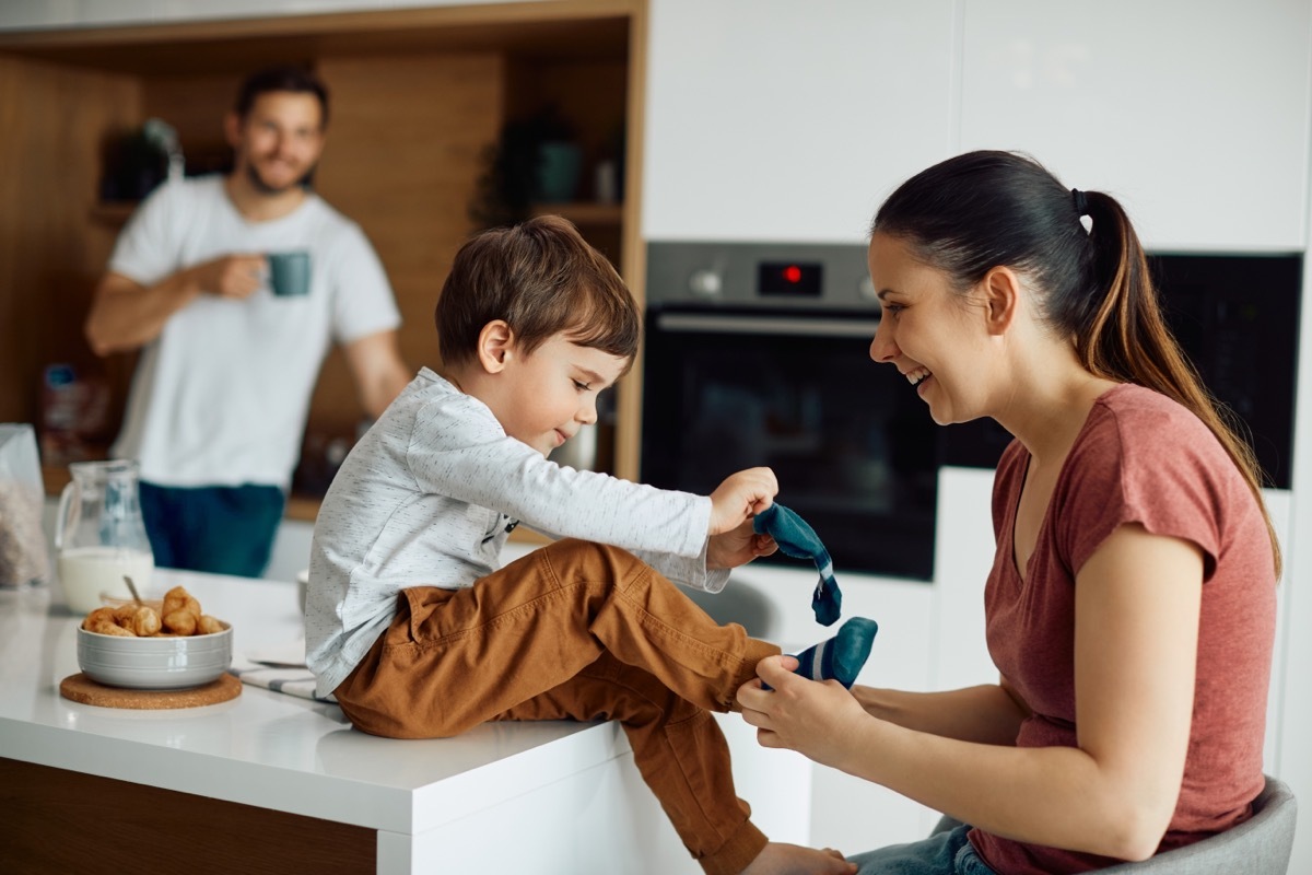 Little boy puts on socks with the help of his mother at home.