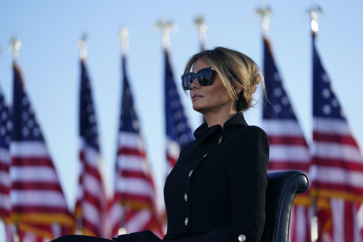 melania trump wears sunglasses while addressing the crowd in front of american flags