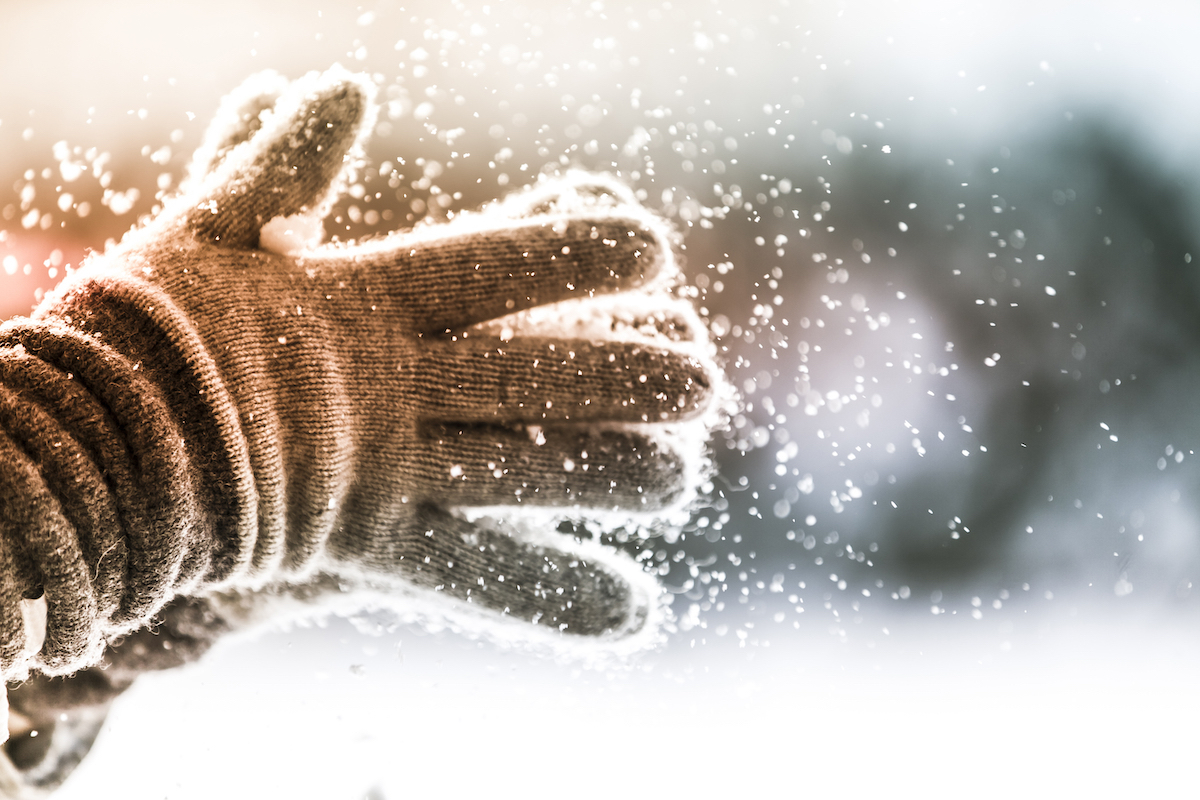 Closeup of person clapping winter gloves together as snow falls from them