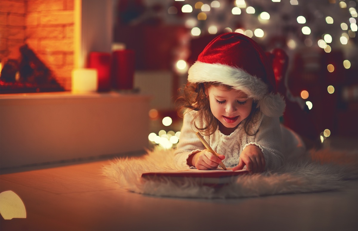 young child writing santa claus a letter in front of a christmas tree