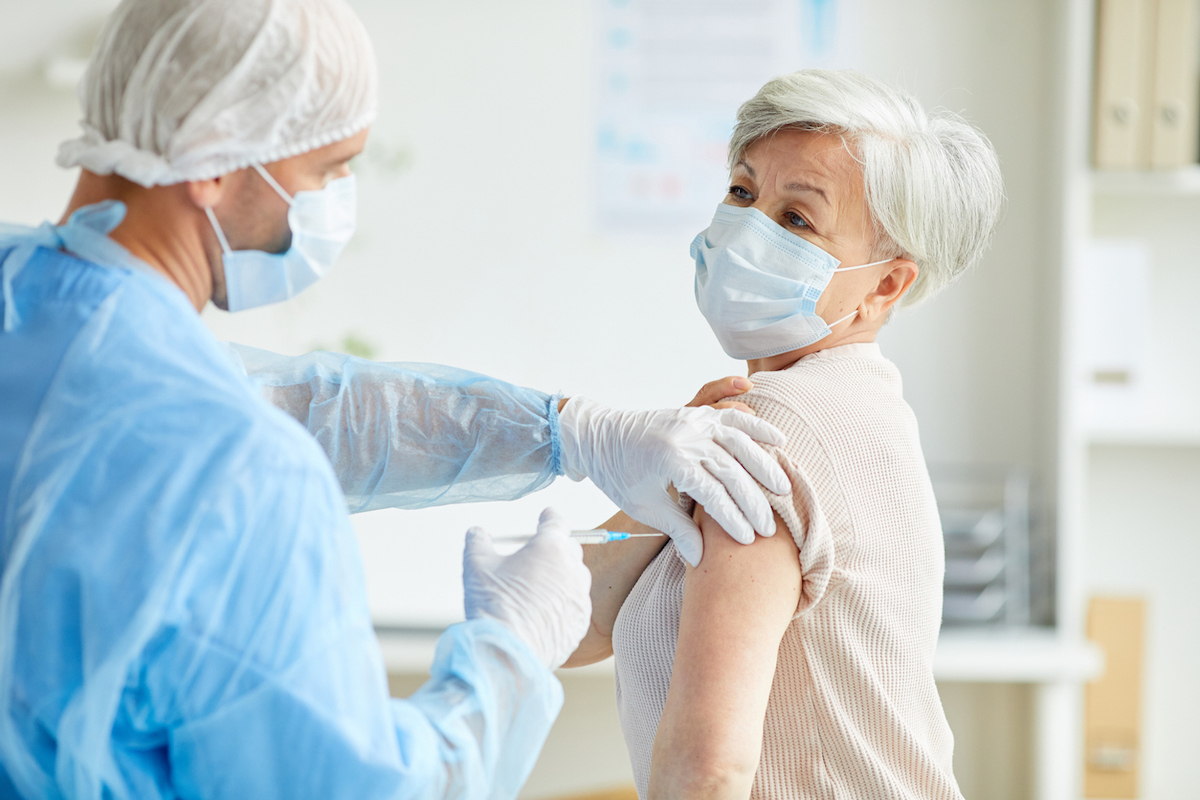 General practitioner wearing protective uniform giving injection with coronavirus vaccine to senior woman