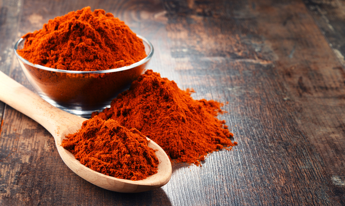 spoon and bowl of cayenne pepper powder on wooden table.