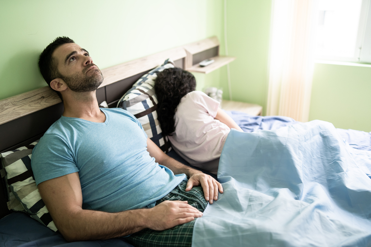 A man and woman sitting in bed during the coronavirus lockdown with the man showing an exasperated look on his face as the woman turns away.