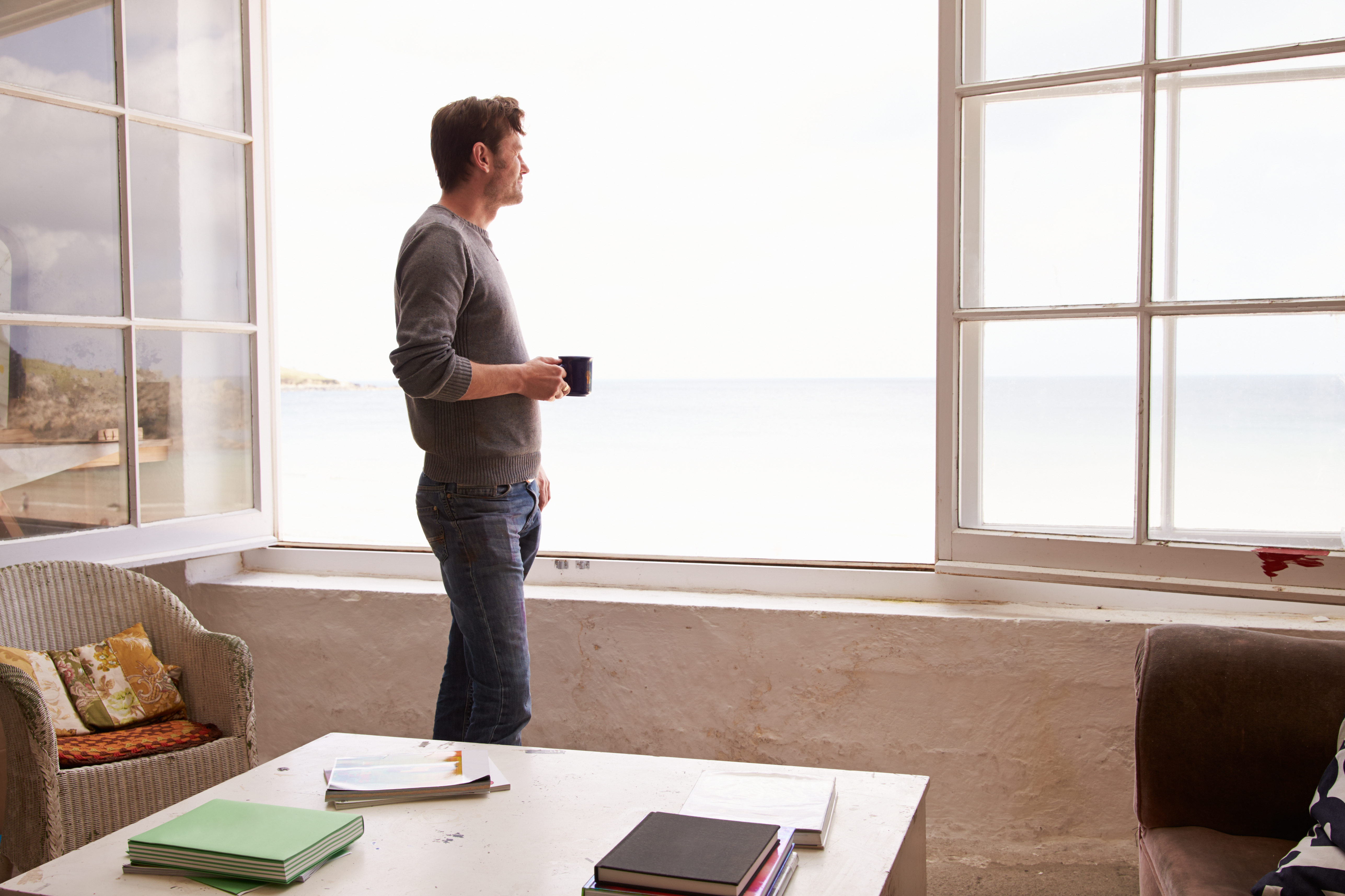 man looking out the window enjoying his morning coffee