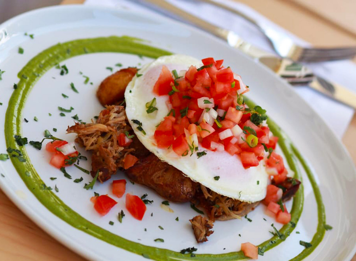 pulled pork underneath an egg with pico de gallo on top surrounded by chimichurri sauce on a white plate from over easy