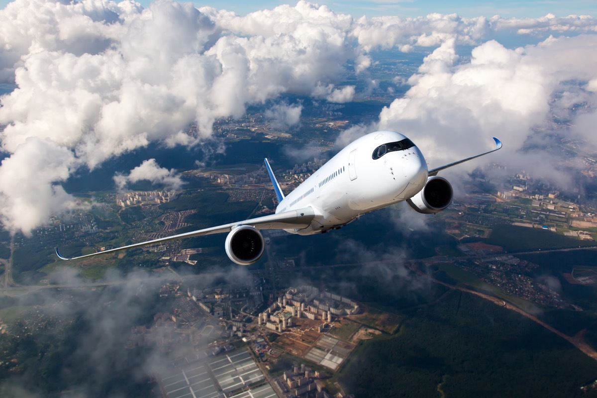 White passenger plane climbs through the clouds. Aircraft is flying high above the city.