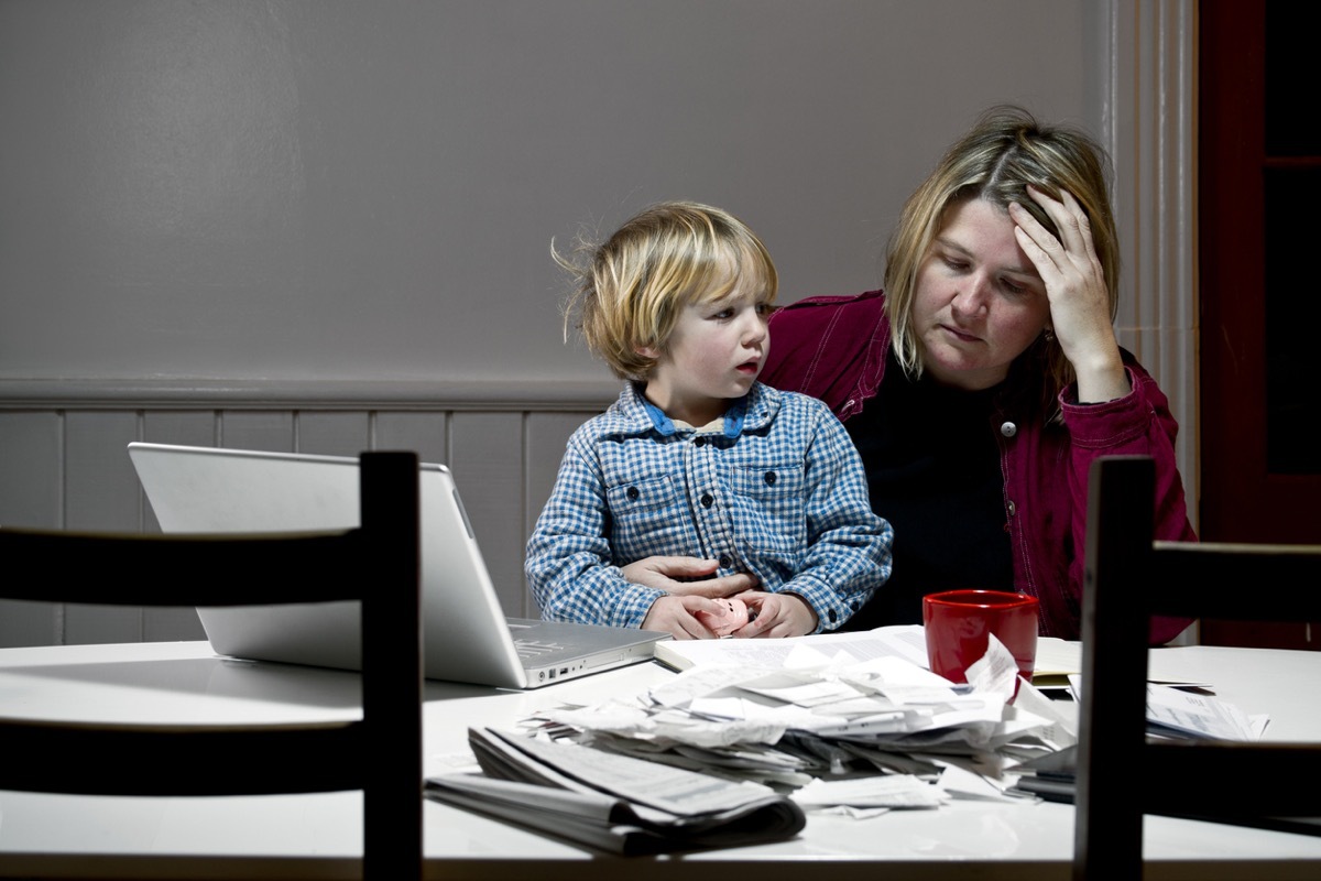 Depressed woman with son in lap at table, overwhelmed with financial issues, debt, bankruptcy.