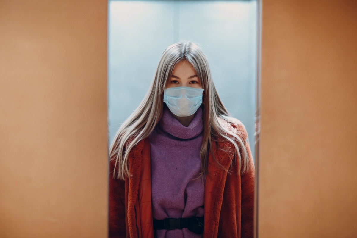 Young chinese woman standing in elevator in medical mask. Doors are closing. Coronavirus COVID-19 pandemic concept.