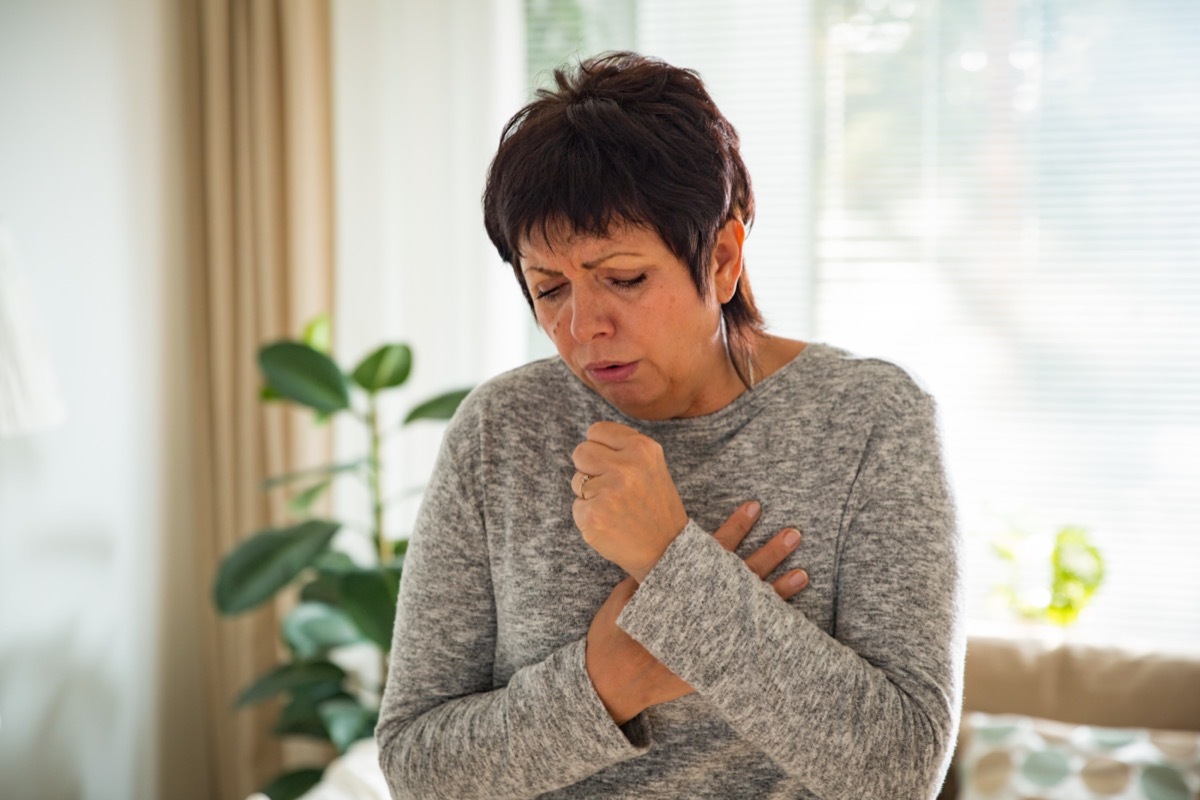 Mature woman with sore throat, standing in living room at home. 