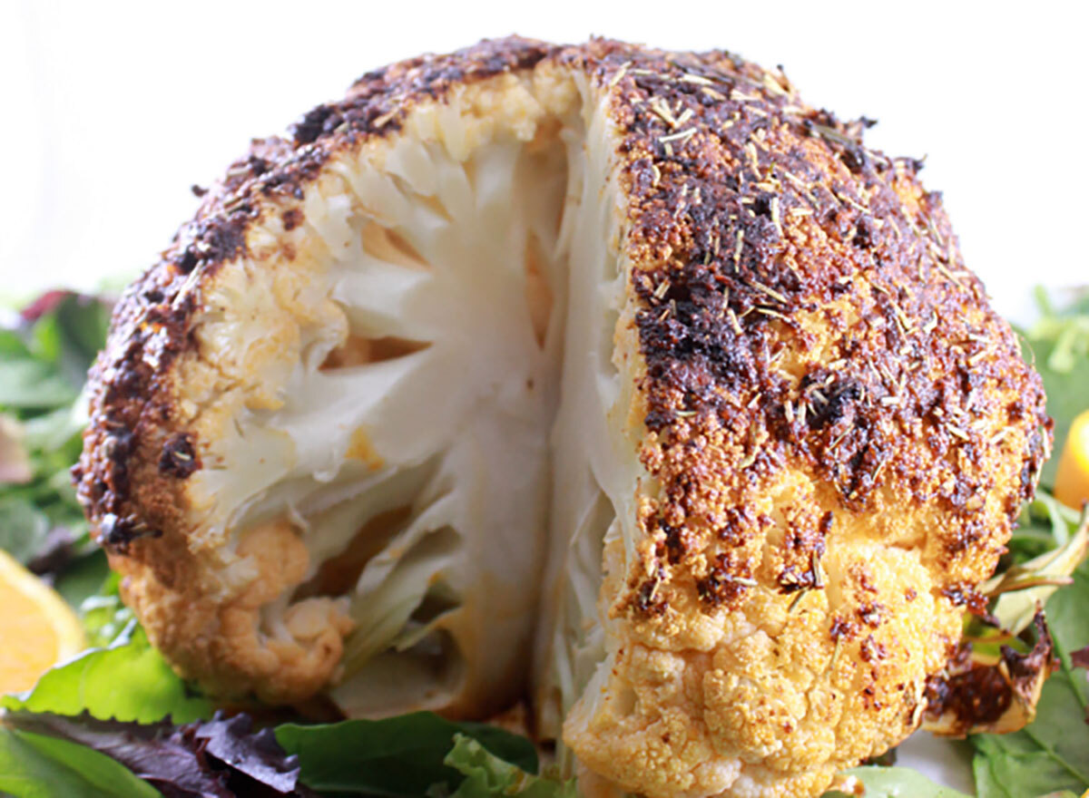 roasted cauliflower head with slice missing on bed of greens