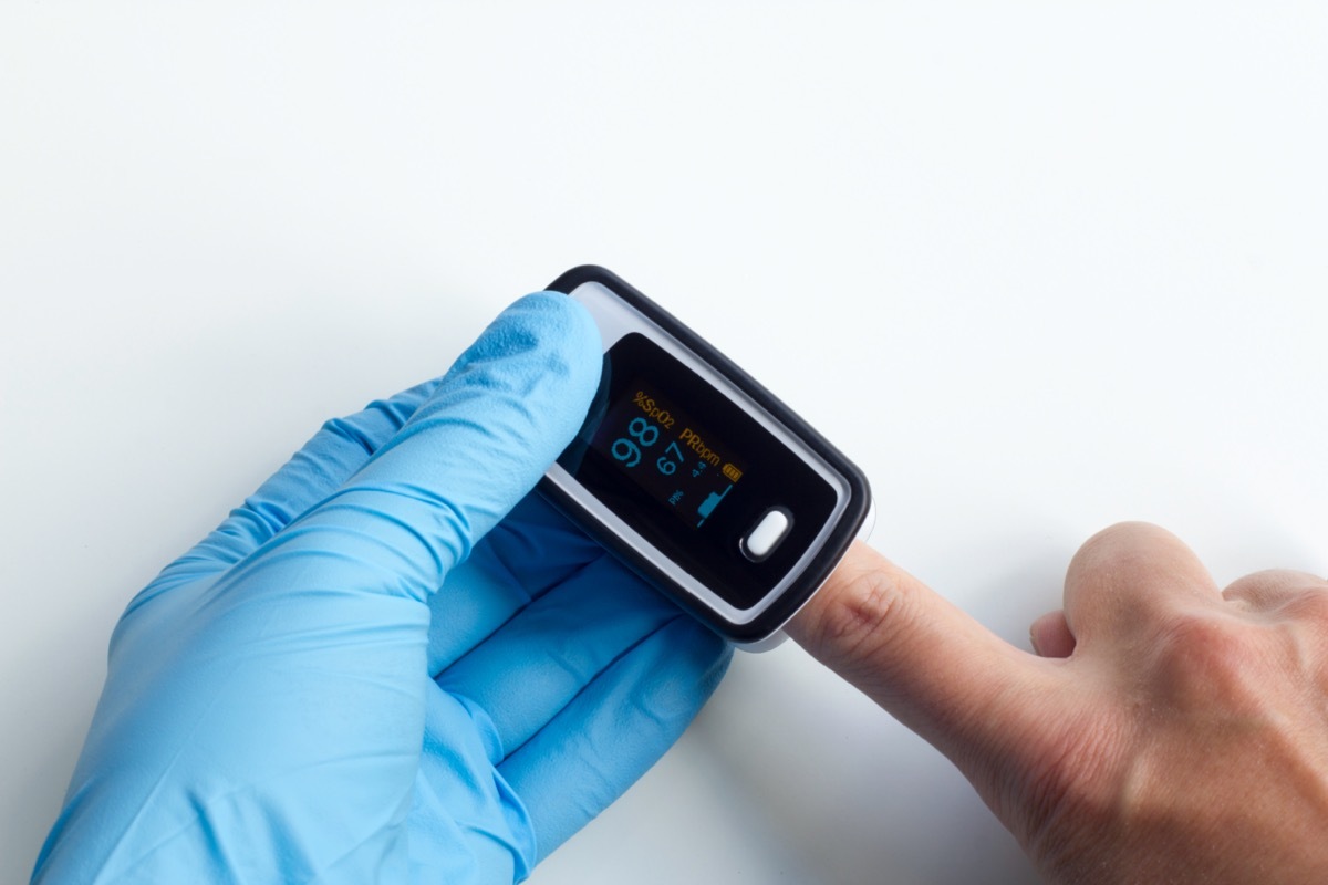 Doctor wearing blue nitrile exam gloves performs a test using a fingertip pulse oximeter to check the patient's oxygen saturation level and pulse rate