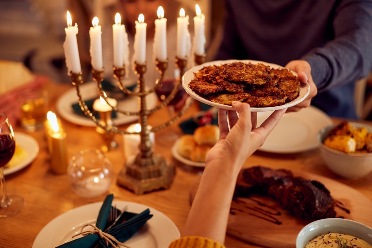 Close-up of couple passing latkes during a meal at dining table while celebrating Hanukkah