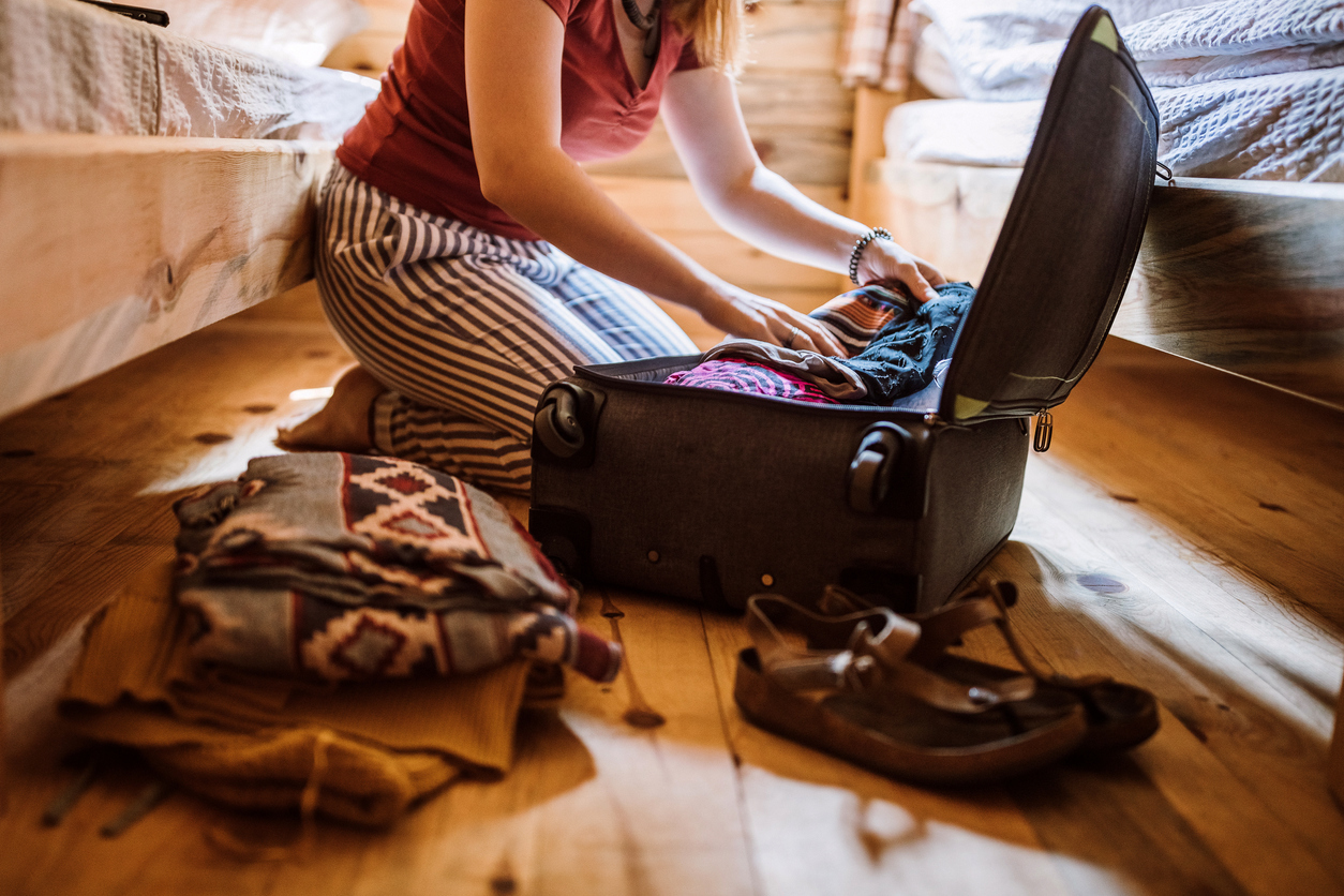 A woman sits on the floor packing her suitcase for a trip next to her bed