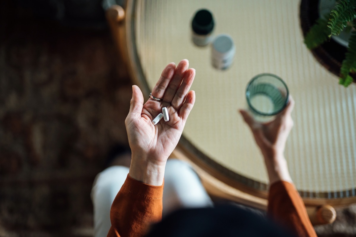 woman feeling sick, taking medicines in hand with a glass of water at home. Elderly and healthcare concept