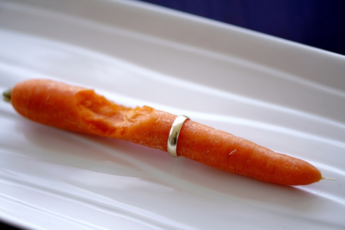 A carrot with a gold ring on it and a bite taken out of the carrot