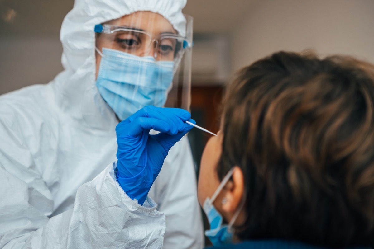 Close up of female health Professional in PPE introducing a nasal swab to a senior female patient at her house. Rapid Antigen Test kit to analyze nasal culture sampling while coronavirus Pandemic.