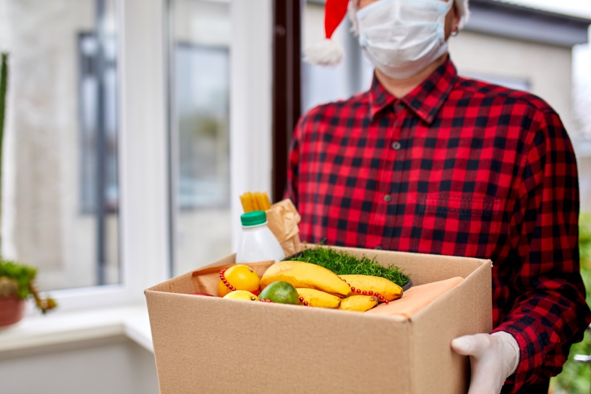 A man holding a box with food while wearing a mask and Santa hat