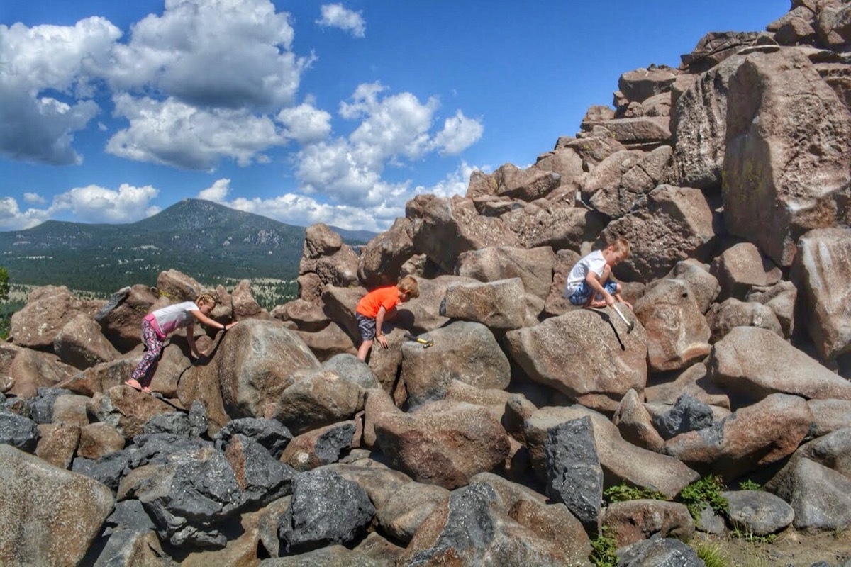 three children climb rocks and hit them with hammers