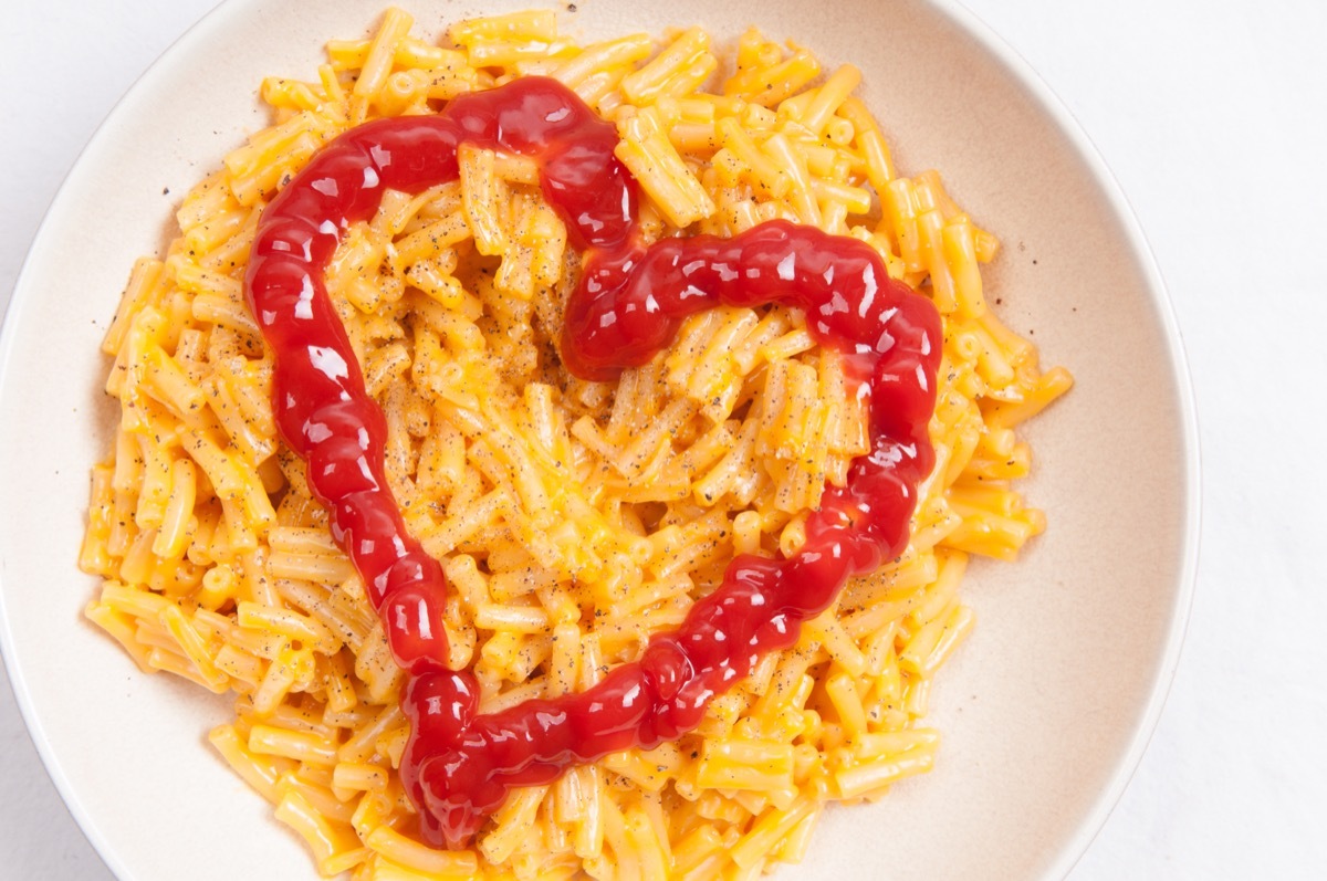 white bowl of macaroni and cheese with a ketchup heart in it