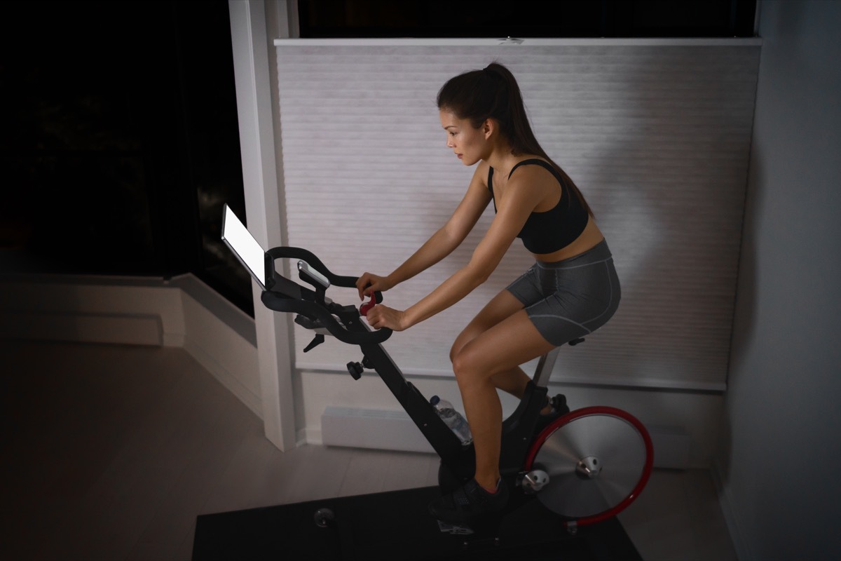 Home workout indoor stationary bike Asian girl biking screen with online classes woman training on smart fitness equipment indoors for cycling exercise. Late at night in bedroom.