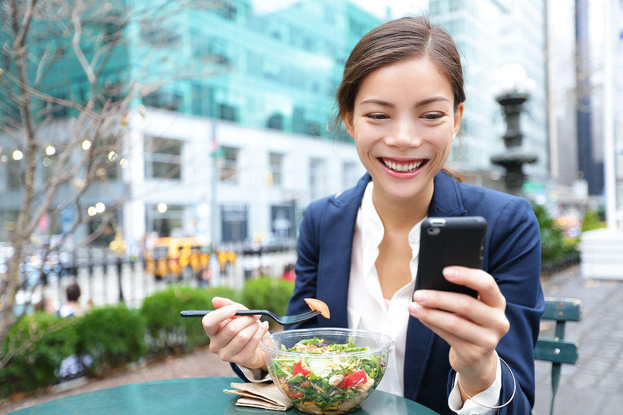 Young business woman eating salad on lunch break in City Park living healthy lifestyle working on smart phone. Happy smiling multiracial young businesswoman, Bryant Park, manhattan, New York City, USA