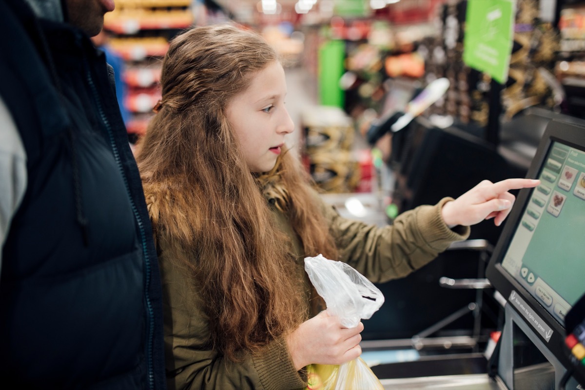 Little girl is at the self service checkout of the supermarket with her father.