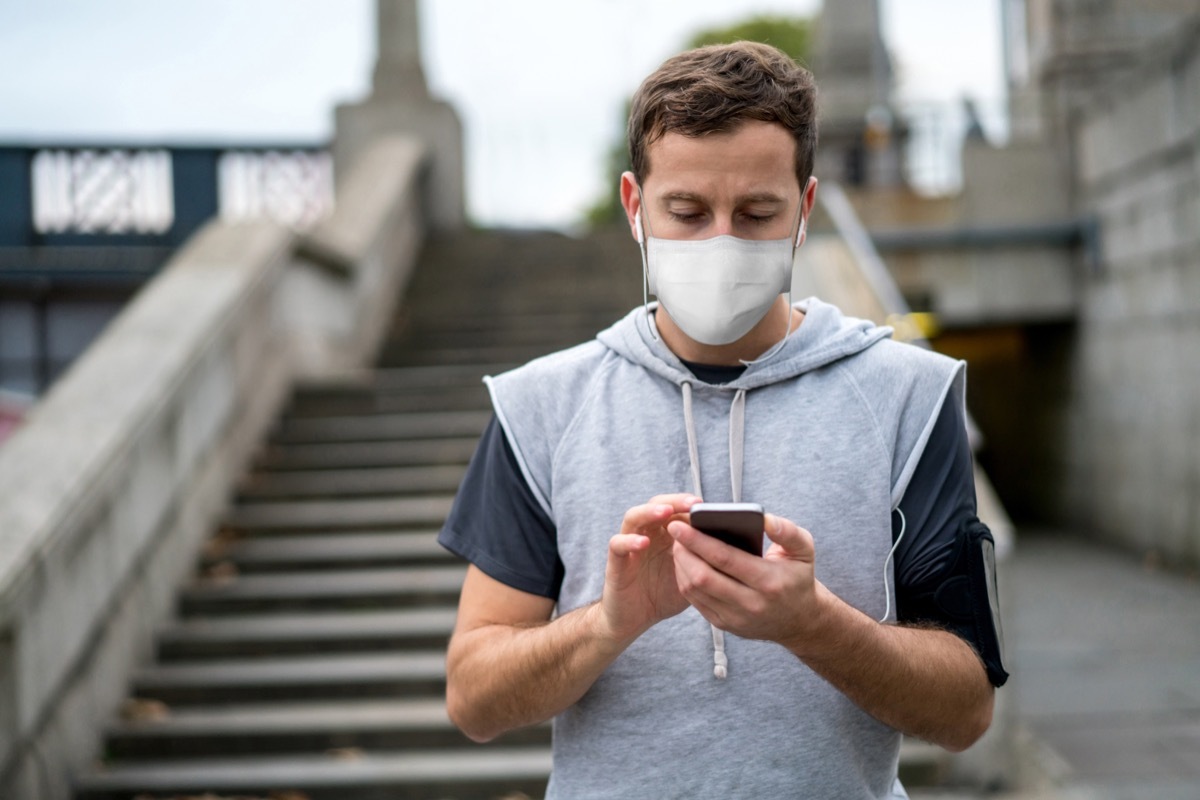 Portrait of a male jogger outdoors wearing a facemask and listening to music while working out in quarantine – COVID-19 lifestyle concepts