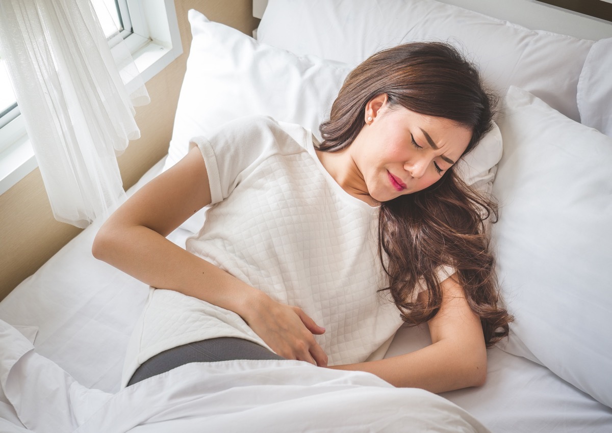 young asian woman in bed with abdominal cramps