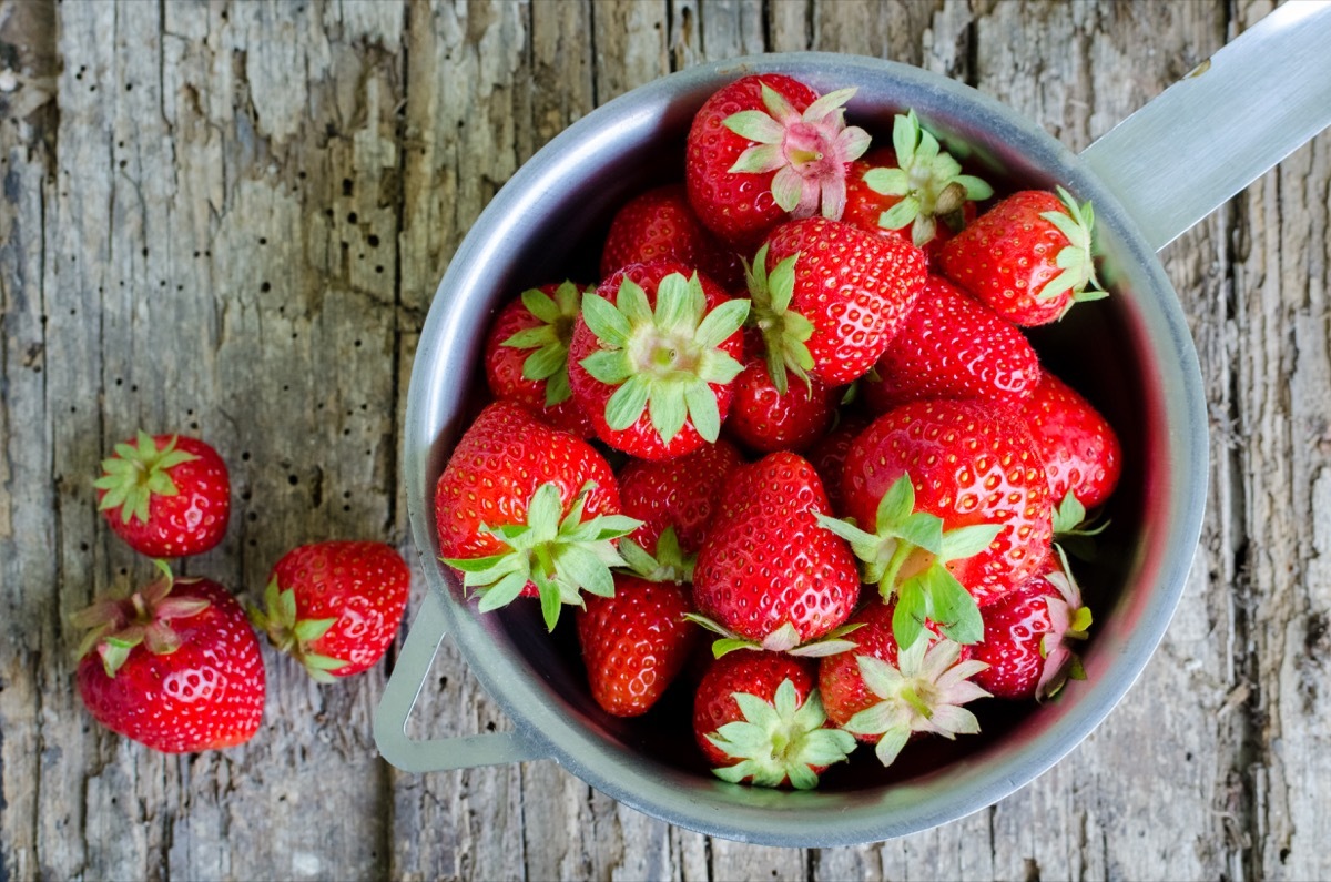 a cup of fresh strawberries on a wooden table