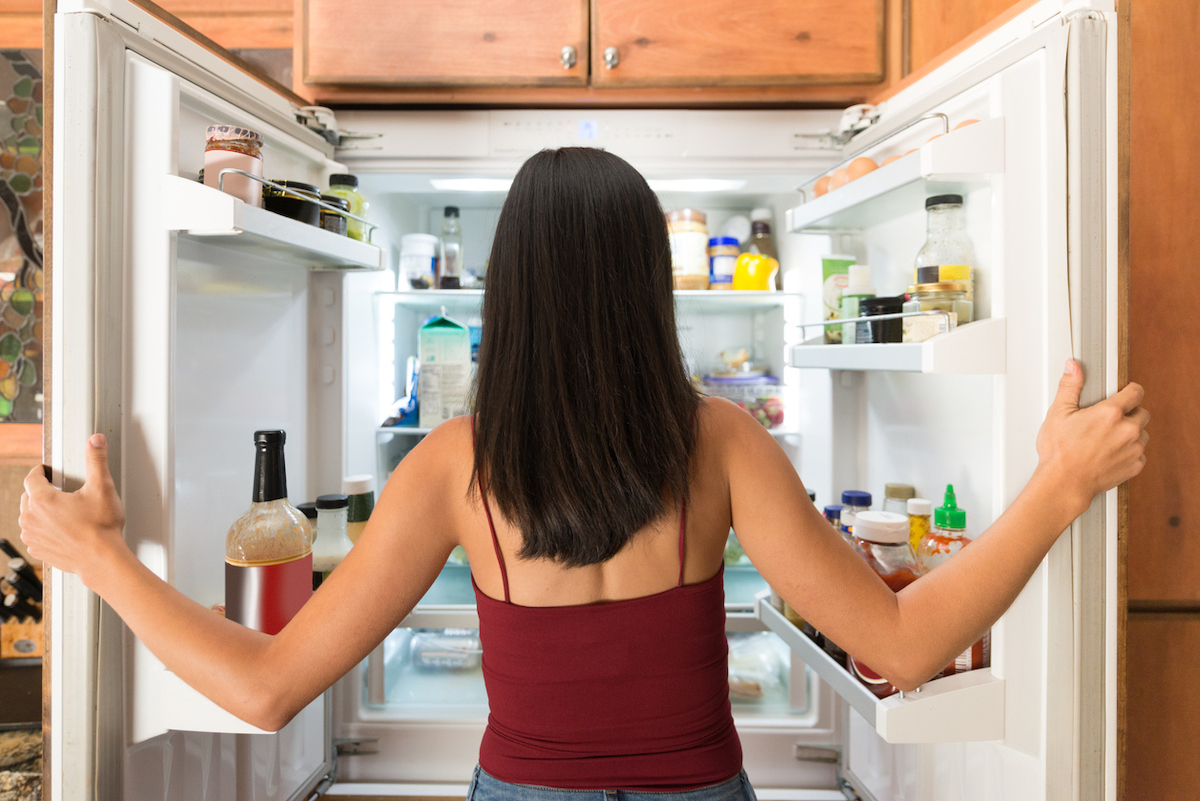 latinx woman in maroon tank top photographed from behind as she looks in the fridge