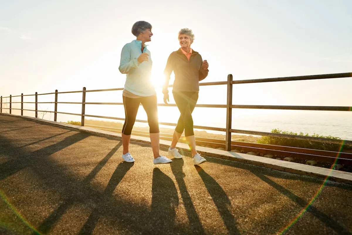 Shot of two senior women walking together in morning with sun shining from behind