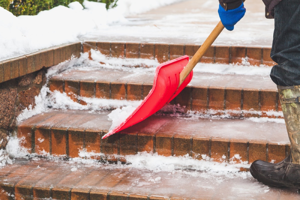 person shoveling snow on brick steps with red shovel