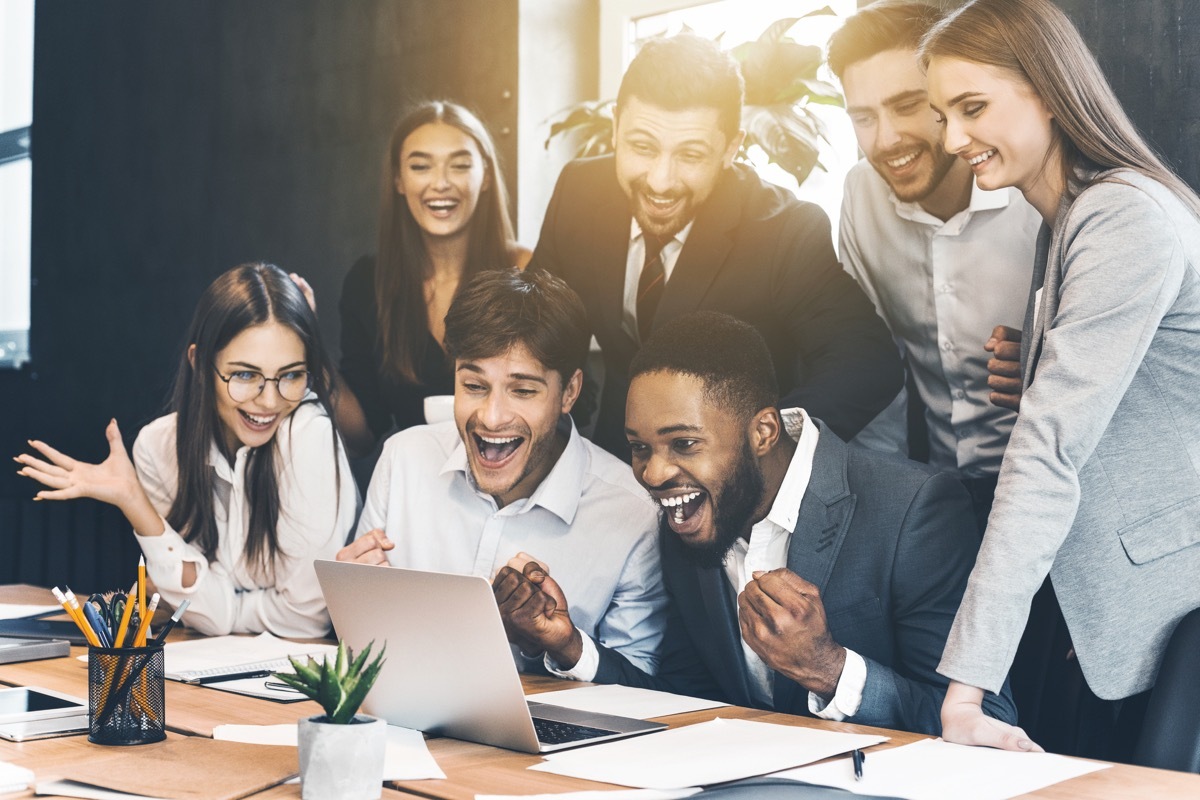 Happy business people celebrating success, looking at laptop screen in the office