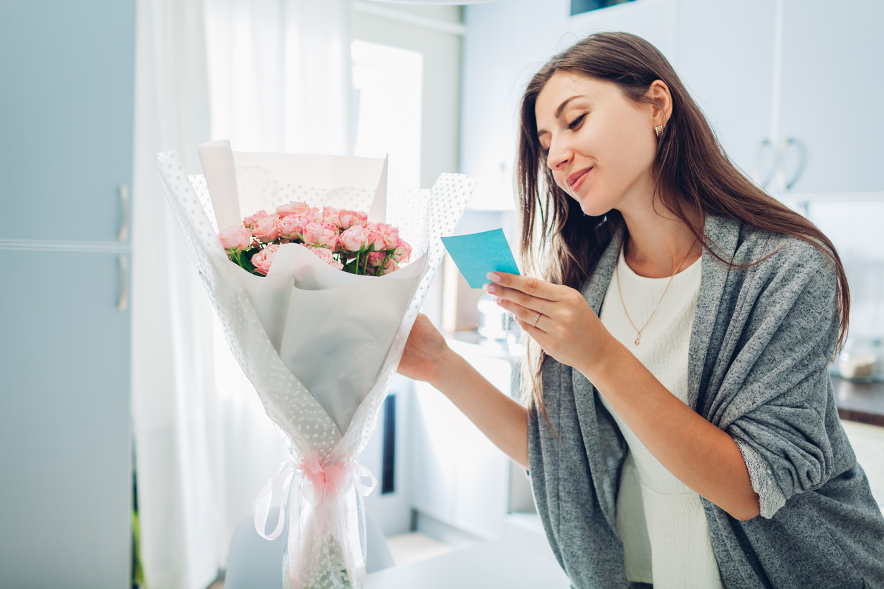 Woman found bouquet of flowers in vase on kitchen and reading card on kitchen. Surprise. Present for holiday