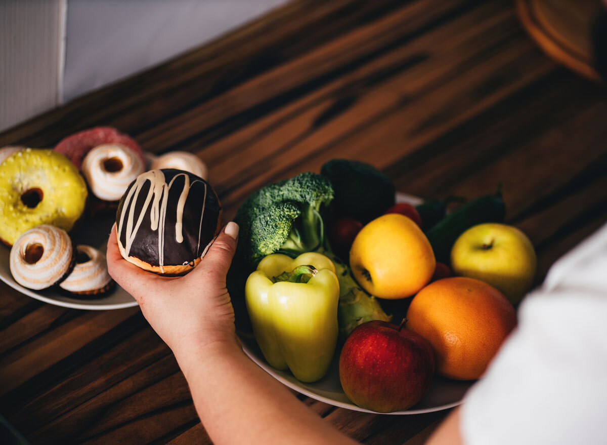 Woman reaching for junk sweet donut instead over fruits and vegetables